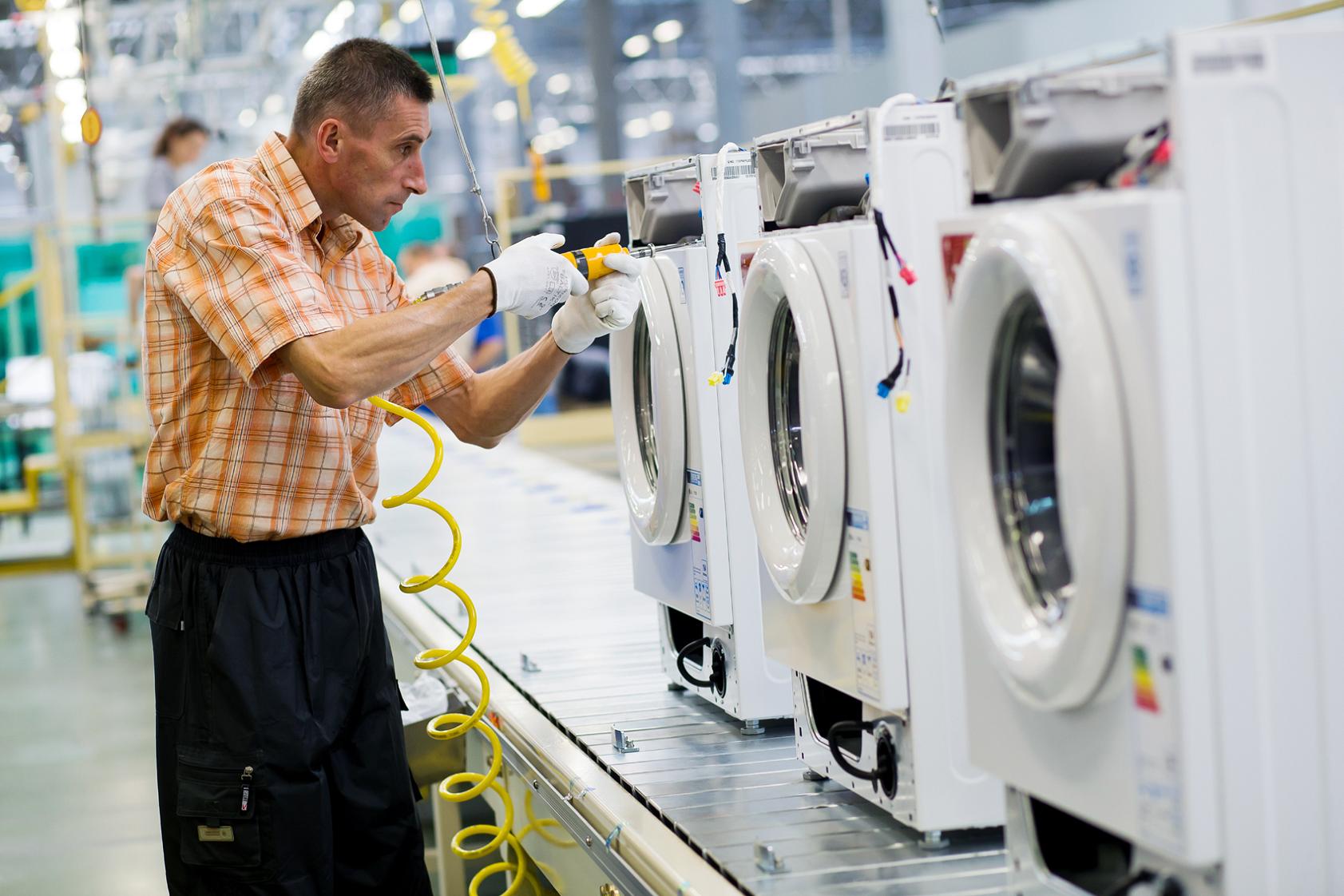 A male worker assembling the compartments of washing machines at an LG factory
