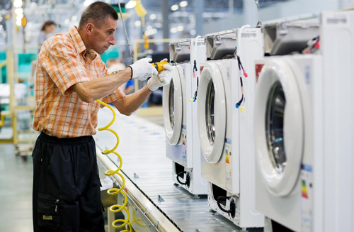 A male worker assembling the compartments of washing machines at an LG factory