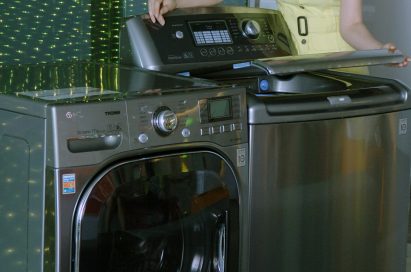 A side view of a woman posing with the LG top-load and front-load washing machines while slightly opening the door of top-loader