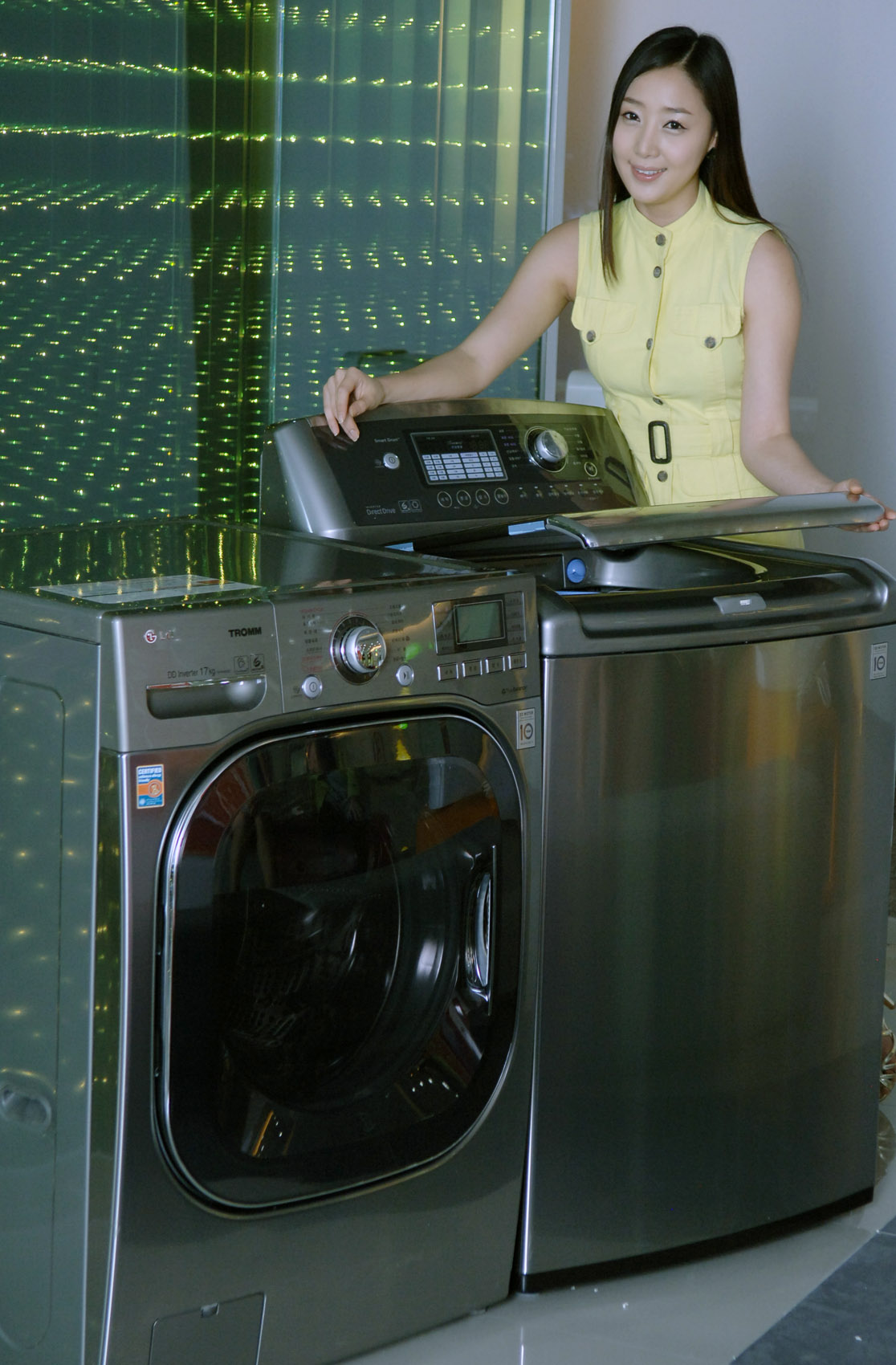 A side view of a woman posing with the LG top-load and front-load washing machines while slightly opening the door of top-loader
