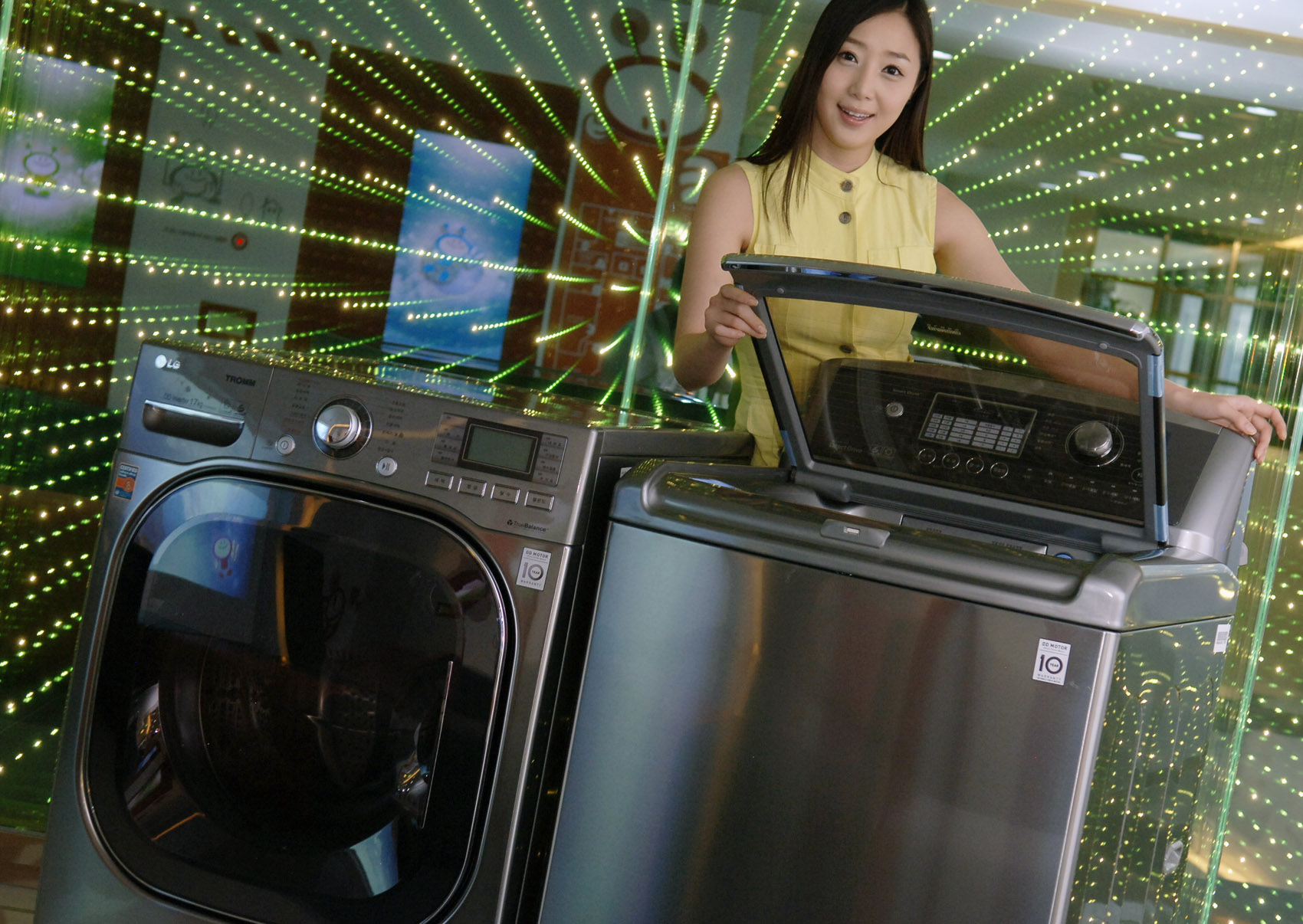 A front view of a woman posing with the LG top-load and front-load washing machines while slightly opening the door of top-loader