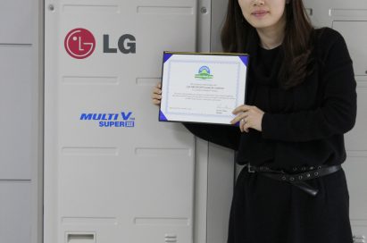 A wider shot of a woman holding up LG MULTI V III’s carbon-free certification letter in front of the air conditioner appliance.