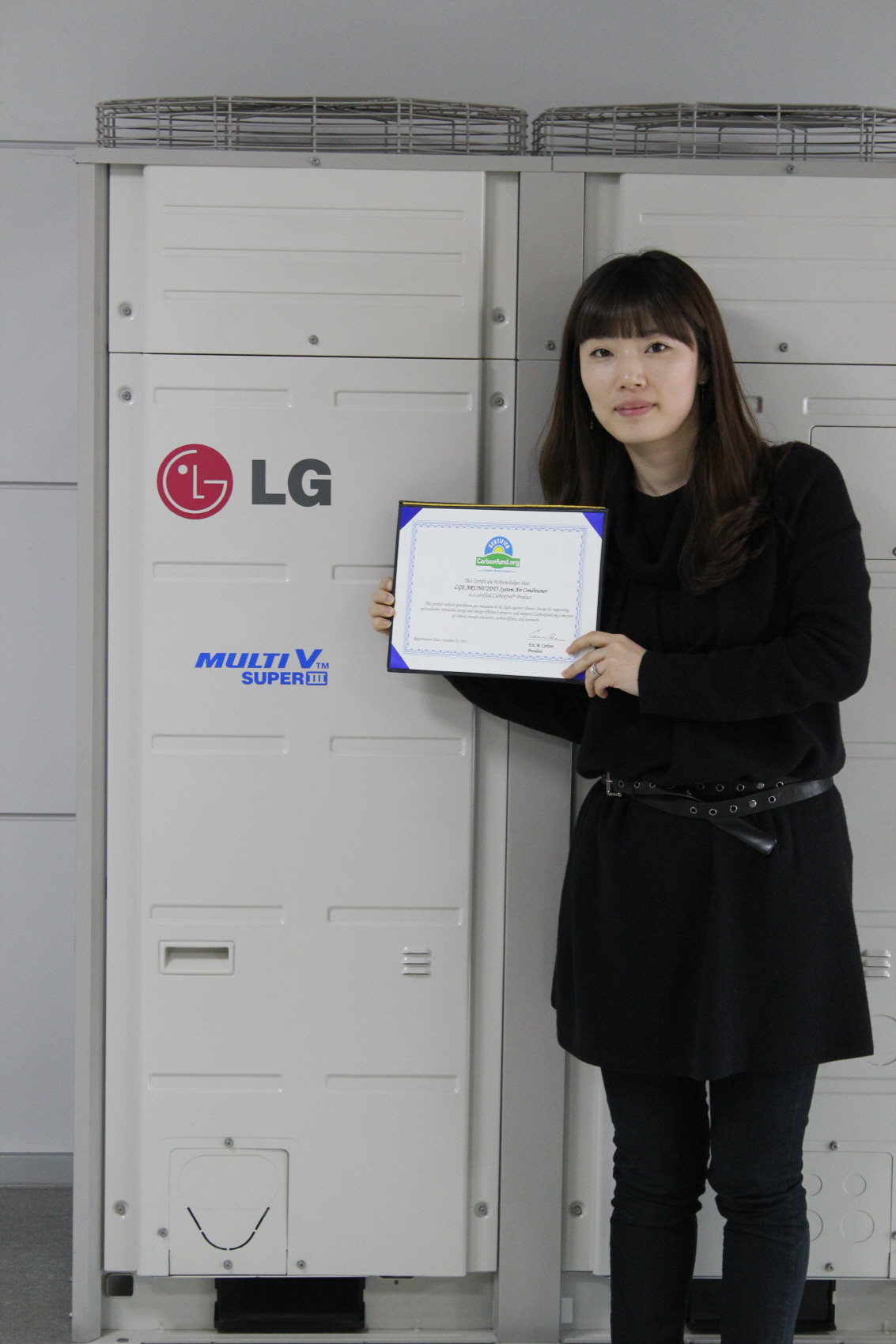 A wider shot of a woman holding up LG MULTI V III’s carbon-free certification letter in front of the air conditioner appliance.