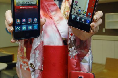 A woman in traditional Japanese clothing holds up two LG Optimus LTEs and shows its front view and LG Optimus LTE showing rear view is displayed in front of her
