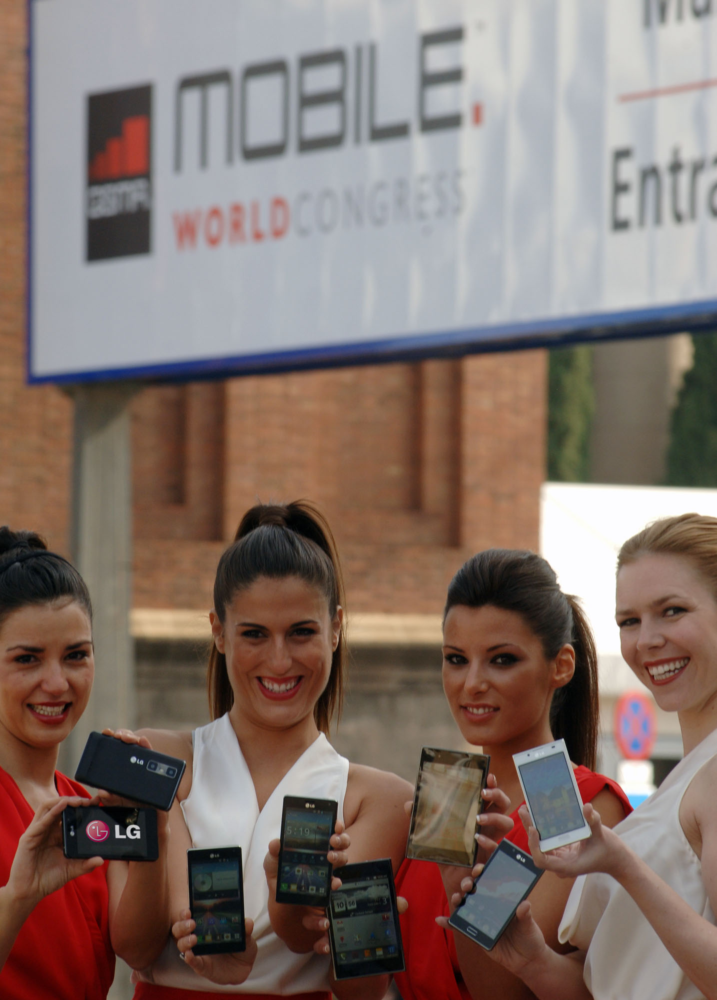 4 female models hold LG Optimus Vu:, LG Optimus 4X HD, LG Optimus 3D Max and LG Optimus L7 and show its front and rear views in front of the main entrance of Fira de Barcelona, Montjuïc venue
