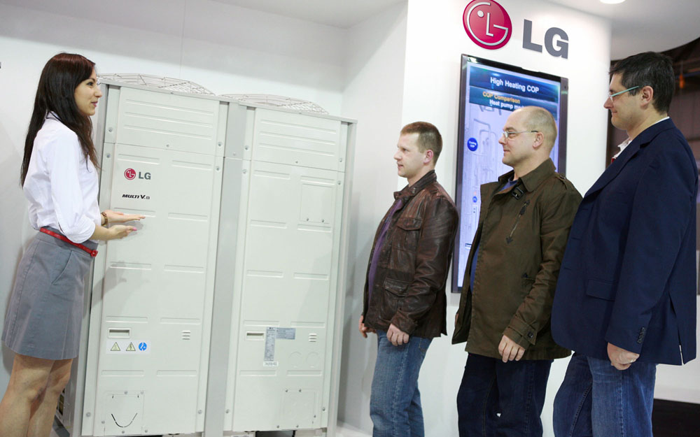 A female attendant explains LG’s Multi V HVAC solution to three men at MCE 2012.