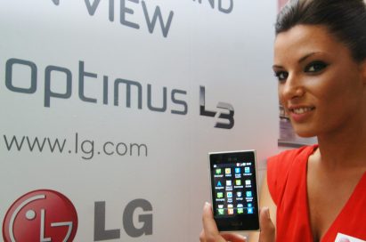 A female model holds two LG Optimus L3s and shows its front views in front of LG Optimus L3 advertisement panel