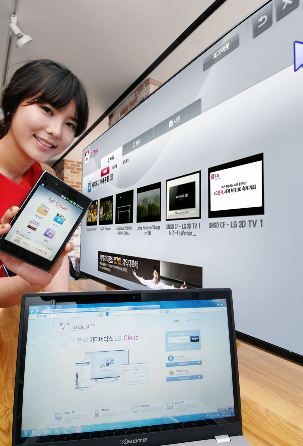 A female model holds up a phone displaying LG Cloud, the company's multimedia cloud platform on the screen while LG's XNote mirrors the phone’s screen.
