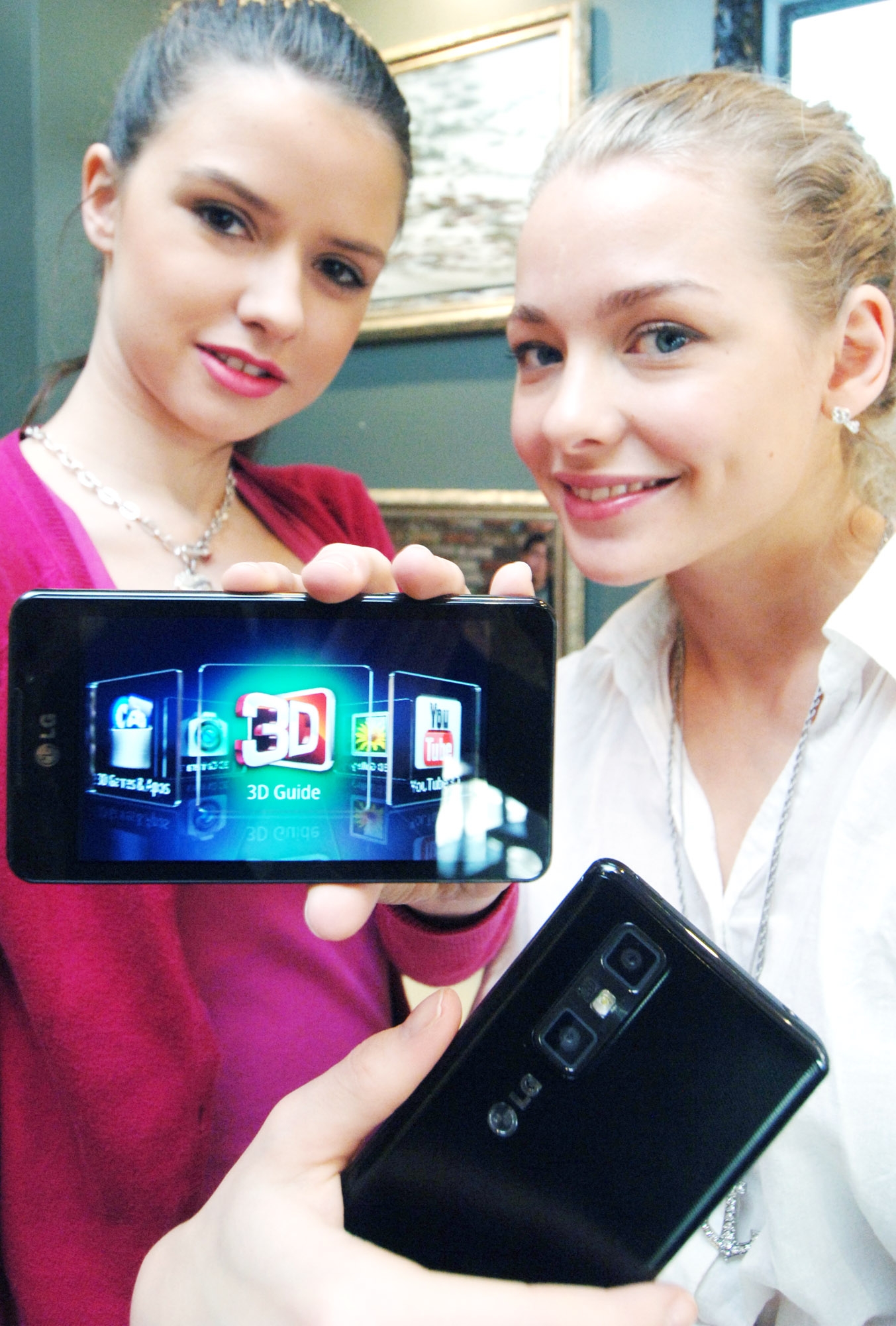 Two female models hold LG Optimus 3D Max and show its front and rear views