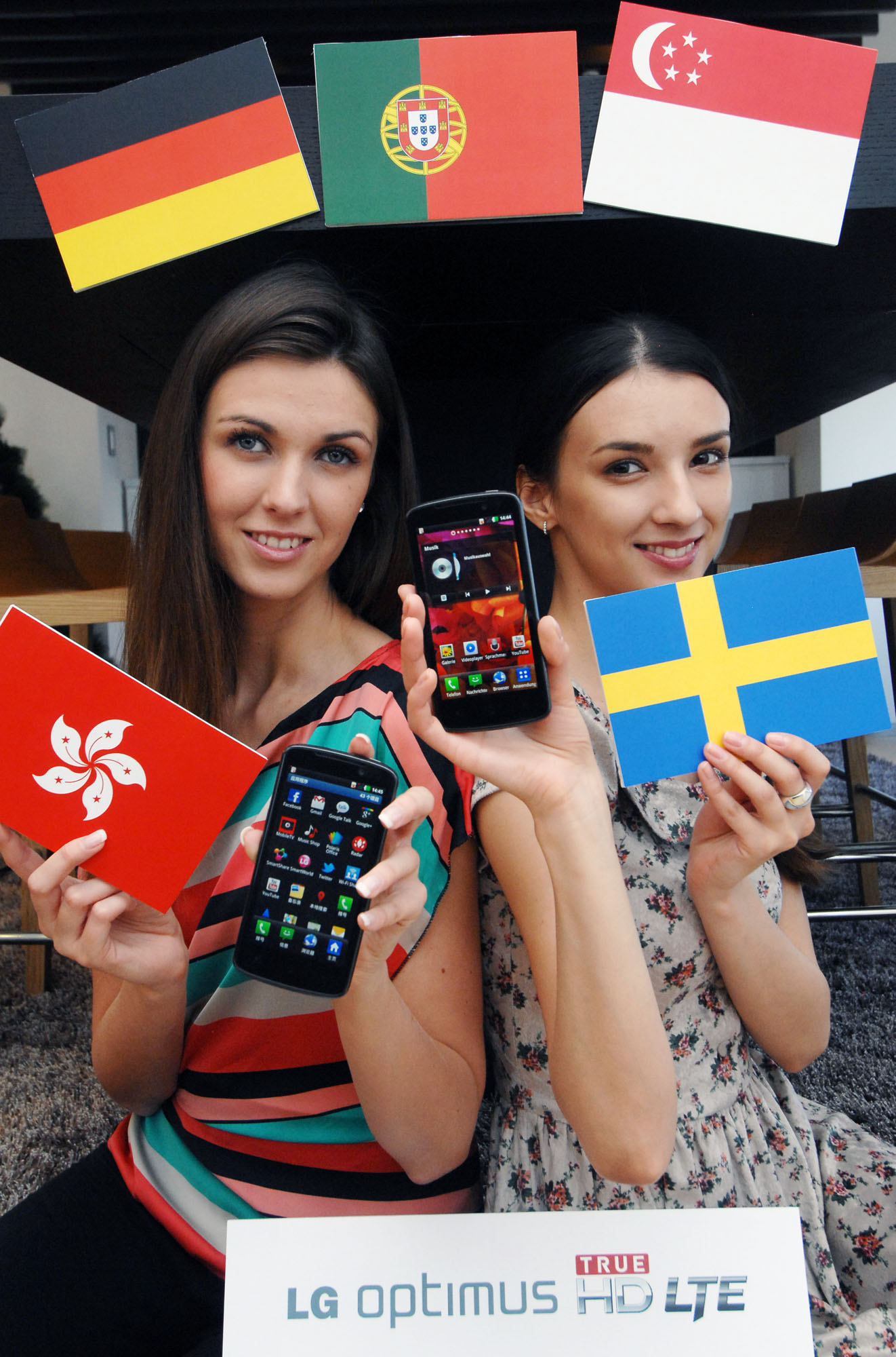 A different view of a model holding a Hong Kong flag and the LG Optimus HD LTE while another holds up the flag of Sweden and another LG Optimus HD LTE, all while in front of the Germany, Portugal and Singapore flags
