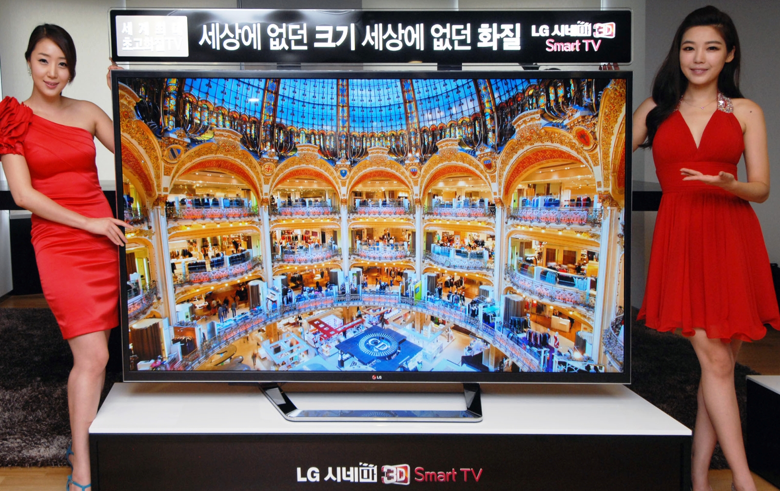 Two models posing at either side of the world’s first 84-inch Ultra Definition 3D TV by LG