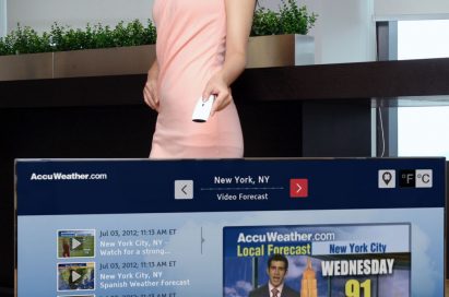 A model controlling an LG Smart TV as it displays a weather forecast channel