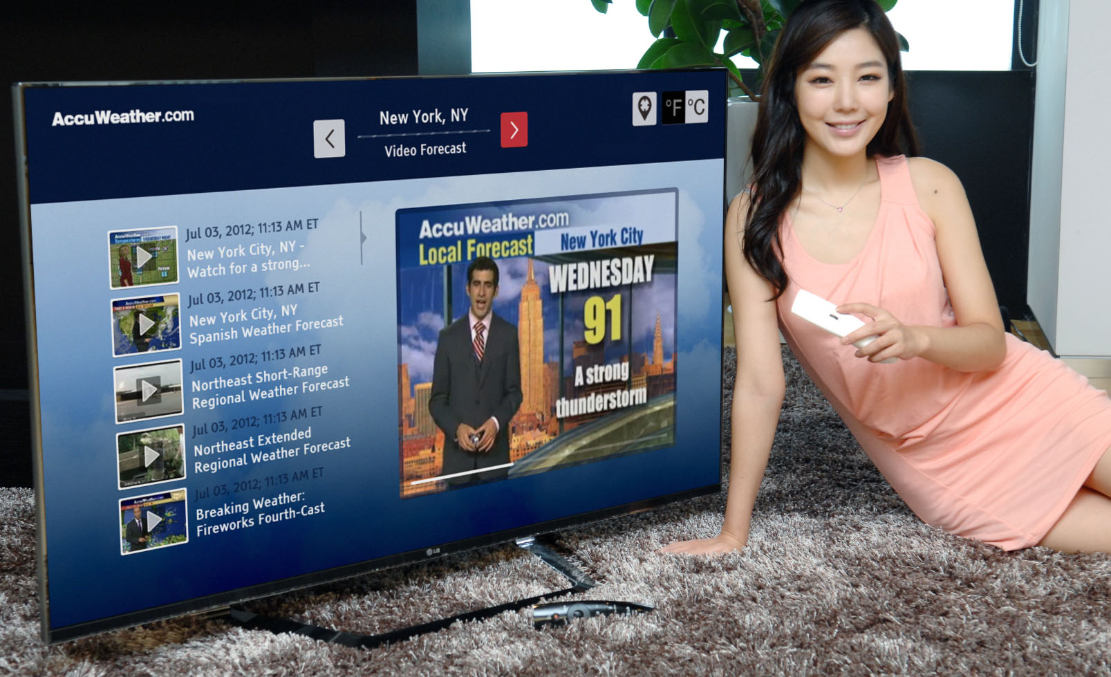 A model lies on the floor while controlling an LG Smart TV as it displays a weather forecast channel