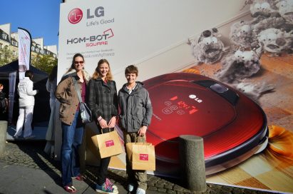 Three visitors pose in front of the LG HOM-BOT advertisement wall