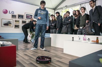 A man controlling LG HOM-BOT with its remote control in front of many visitors