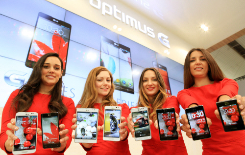 LG's Optimus Series_G, Vu:, F and LII (1) Four female models are smiling at a camera holding various strategic Optimus series devices at MWC 2013 - G, Vu:, F and LII.