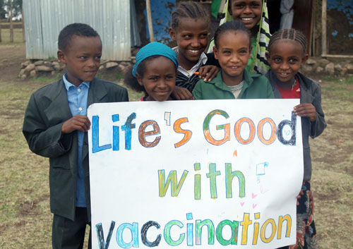 Children smile for the camera with a "Life's Good with vaccination" sign