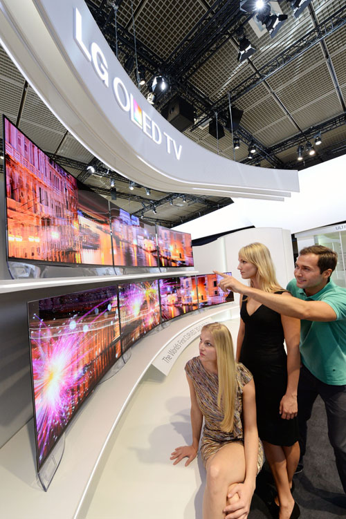 Three visitors view two rows of LG’s CURVED OLED TVs on show at IFA 2013.