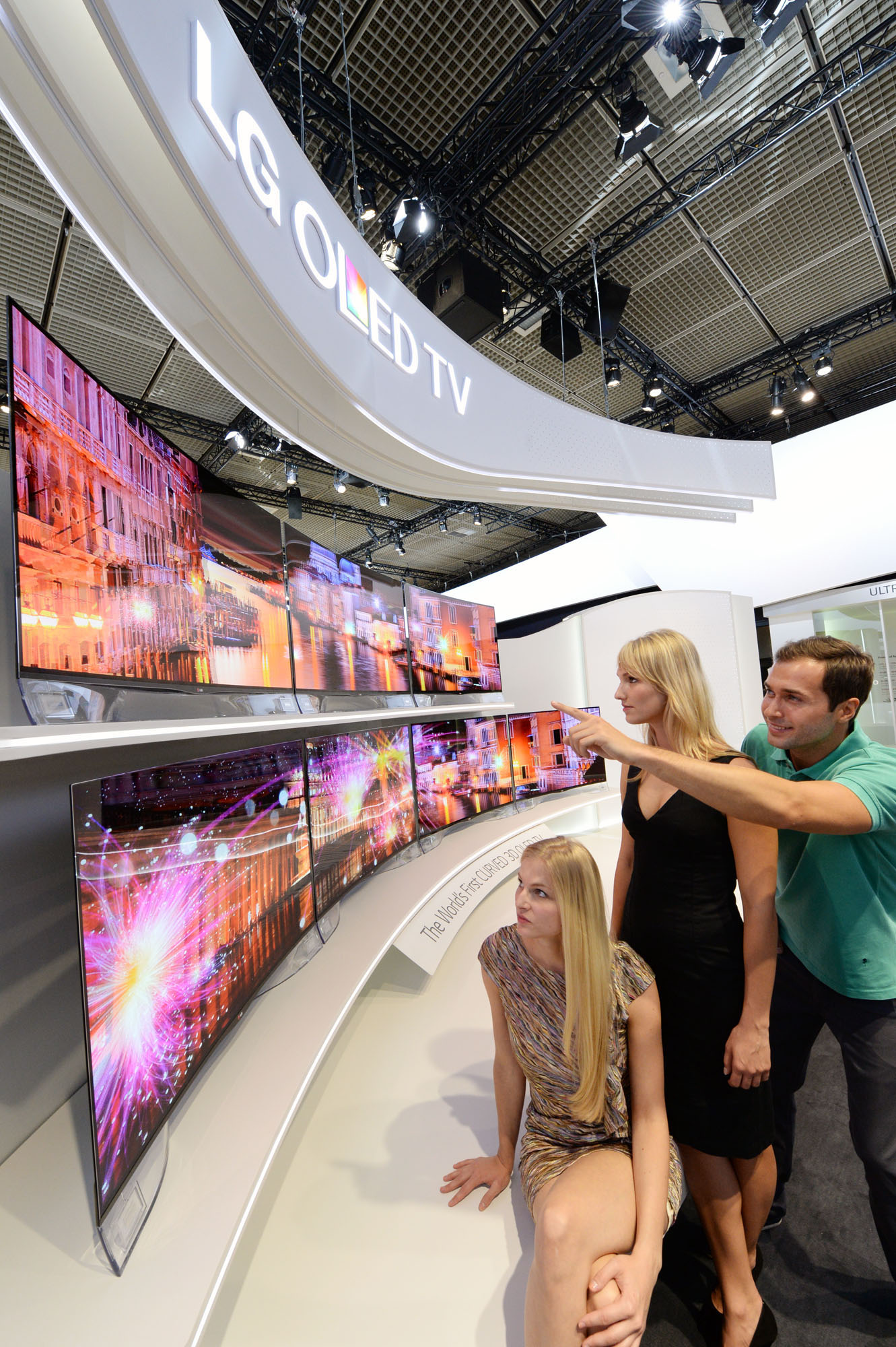 Three visitors view two rows of LG’s CURVED OLED TVs on show at IFA 2013