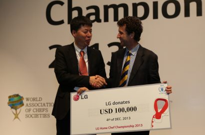 An LG representative shakes hands with a gentleman from the United Nations World Food Programme (WFP) while holding a panel showing LG’s donation of 100,00 USD at the LG Home Chef Championship 2013
