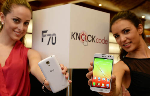 From left to right; A female model is holding a LG F70 in white color to show its back and another model is trying to show its front.