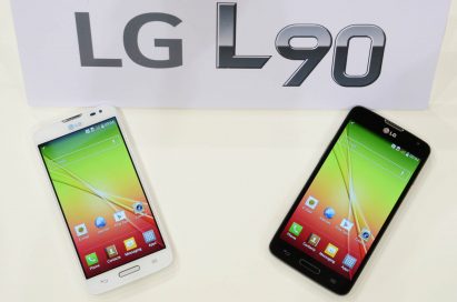 Two LG L90s, each in white and black color, are lying on a table and a panel with the logo of LG L90 on is standing on the table.