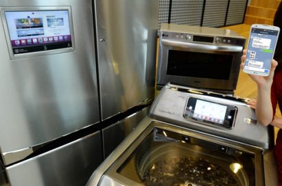 LG’s smart appliances including its Multi-Door refrigerator, top-load washing machine and light wave oven, with a model holding a smartphone with the LG HomeChat™ application open.