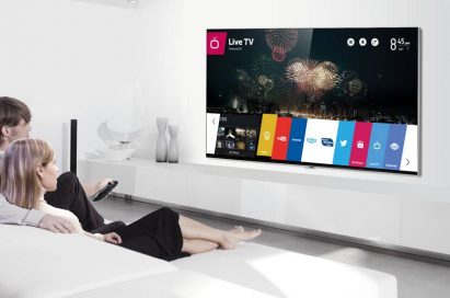 A man and woman sit on their sofa while selecting apps run by webOS with a remote on the LG Smart+ TV