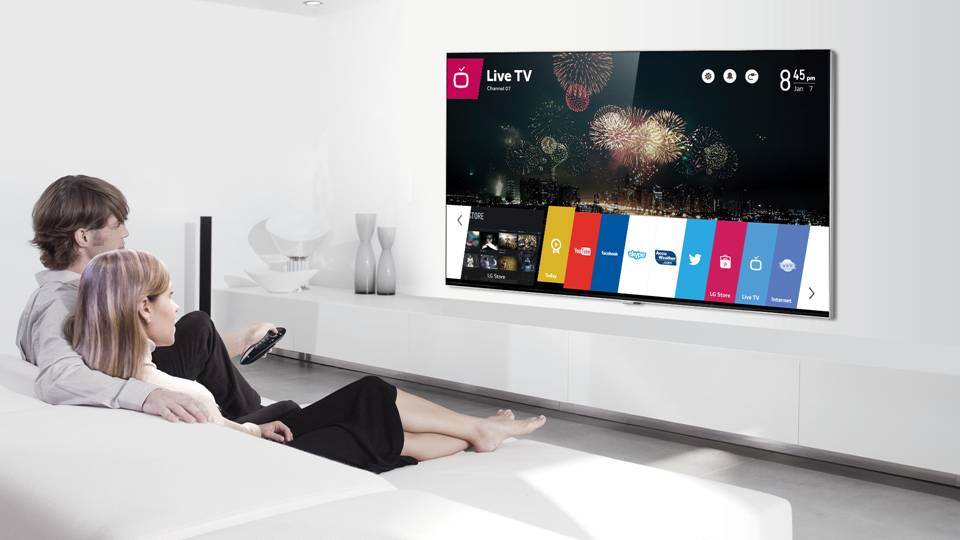 A man and woman sit on their sofa while selecting apps run by webOS with a remote on the LG Smart+ TV