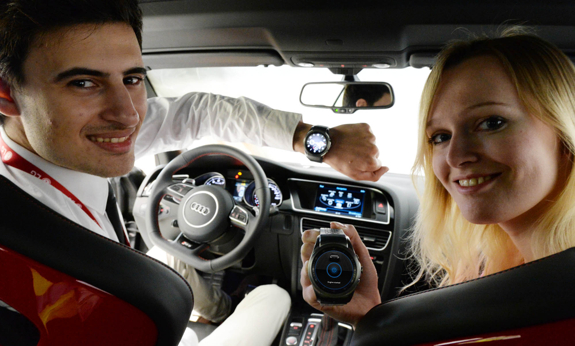 Two models sit in a car, the man wearing the LG Watch Urbane and woman holding one while posing for the camera