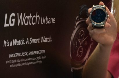 A woman holds the LG Watch Urbane in front of an large poster for the watch.