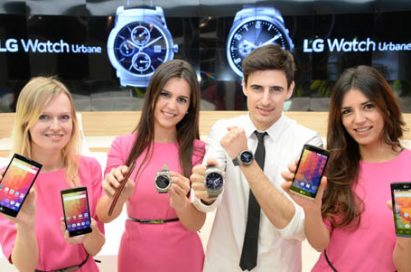 Four models are smiling at a camera holding LG smartphones and LG Watch Urbane at LG booth of MWC.