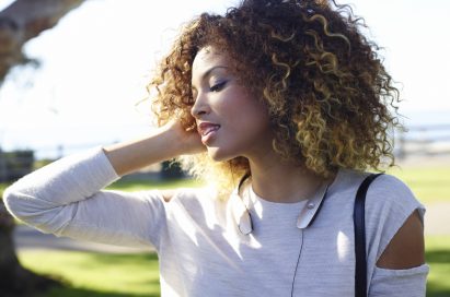 A woman enjoying music with the LG TONETM Bluetooth headset at a park.