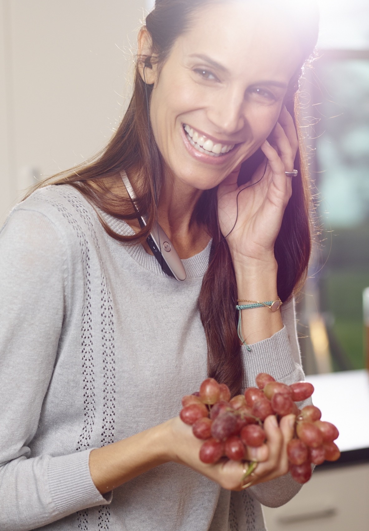 A woman talking on her phone through a LG TONETM Bluetooth headset while holding grapes in her hand.