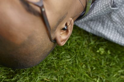A man enjoying music with the LG TONETM Bluetooth headset while lying in the grass.