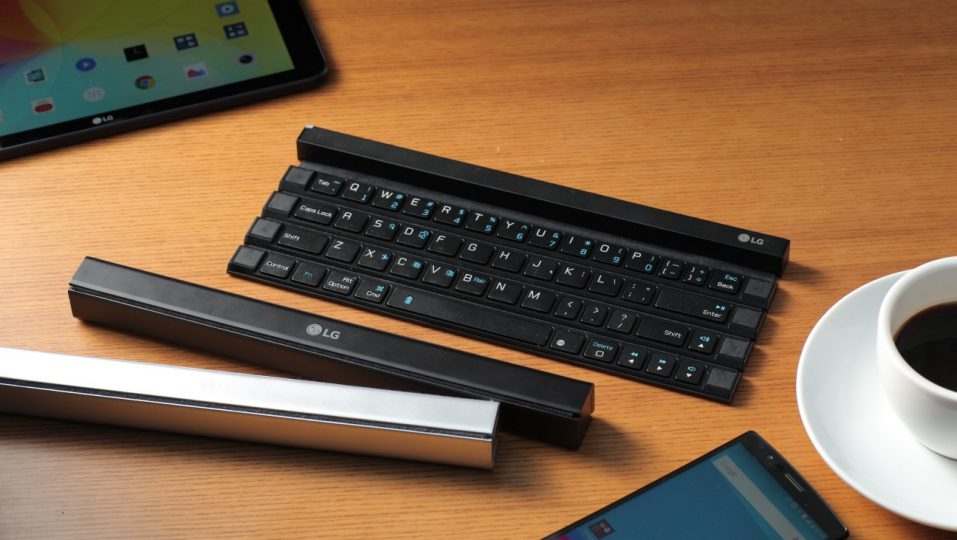 Three Rolly Keyboards displayed on the table with a G pad, an LG smartphone and a cup of coffee. Two of them are folded up with the other is ready to use.