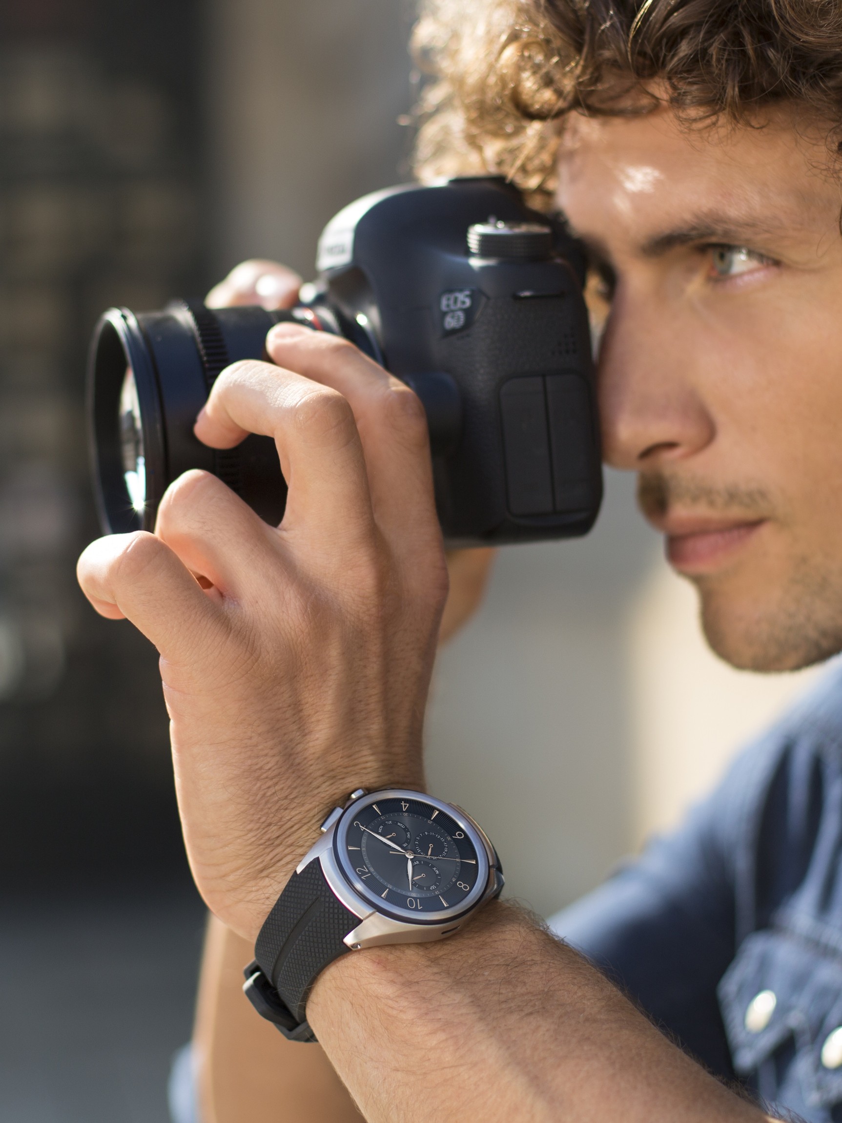 A man with the LG Watch Urbane 2nd Edition on his wrist takes a photo with a DSLR camera