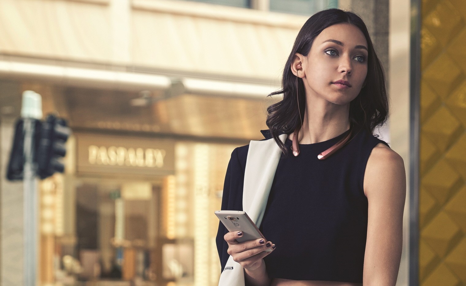 A woman with the LG TONE Infinim™ in Rose Gold around her neck and the retractable ear buds in her ears