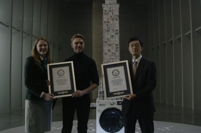 Three people holding Guinness World Record certification in front of LG Centum System™ washing machine with house of card built on it