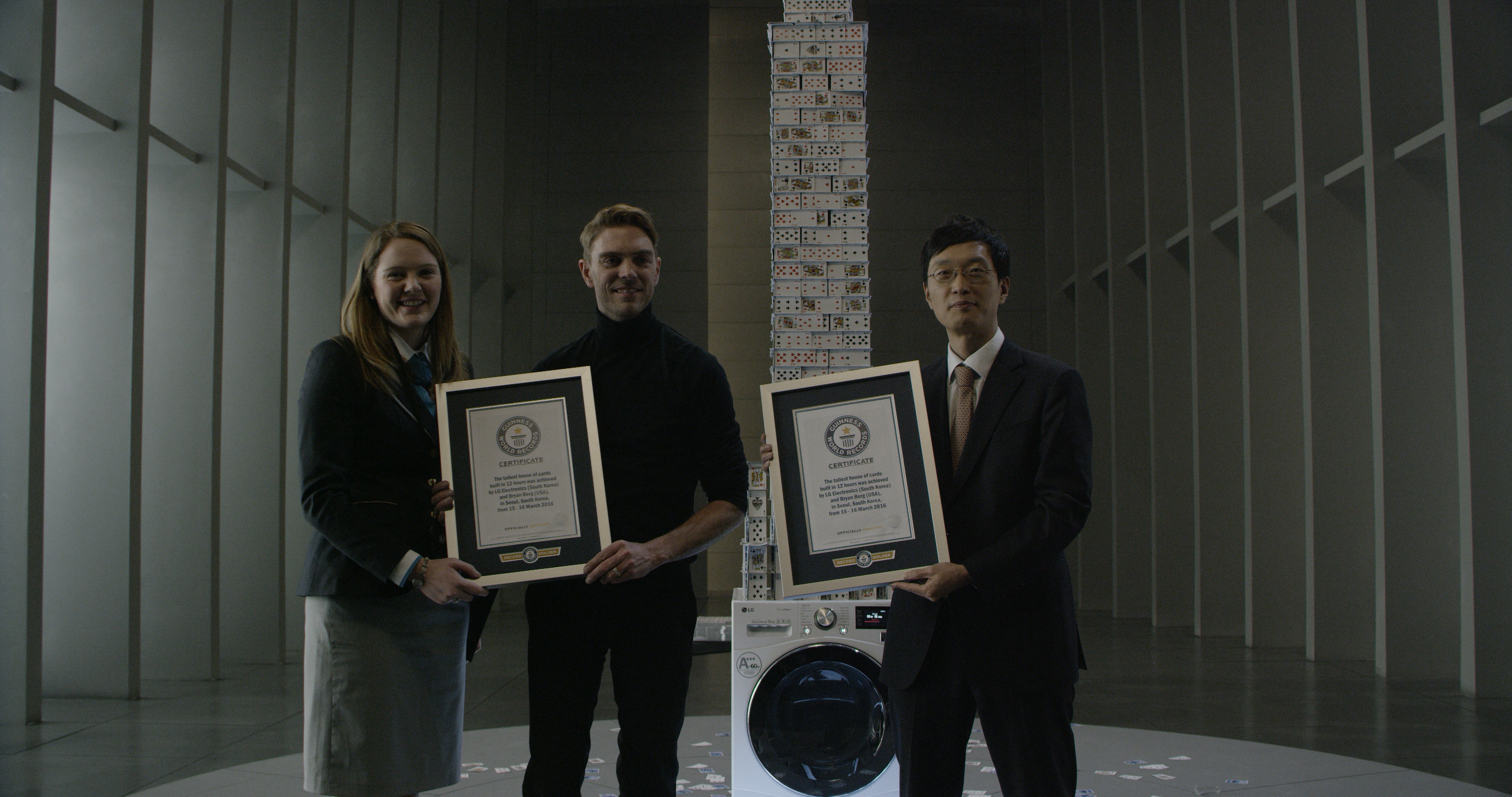 Three people holding Guinness World Record certification in front of LG Centum System™ washing machine with house of card built on it