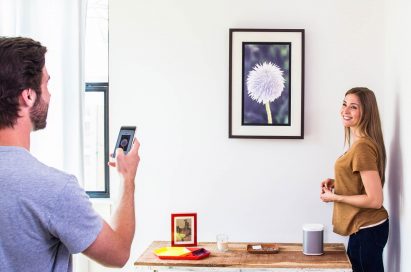 A man uses art streaming platform, Acanvas, to connect his phone to one of its cord-free customizable digital frames, while a woman oversees with a smile on her face