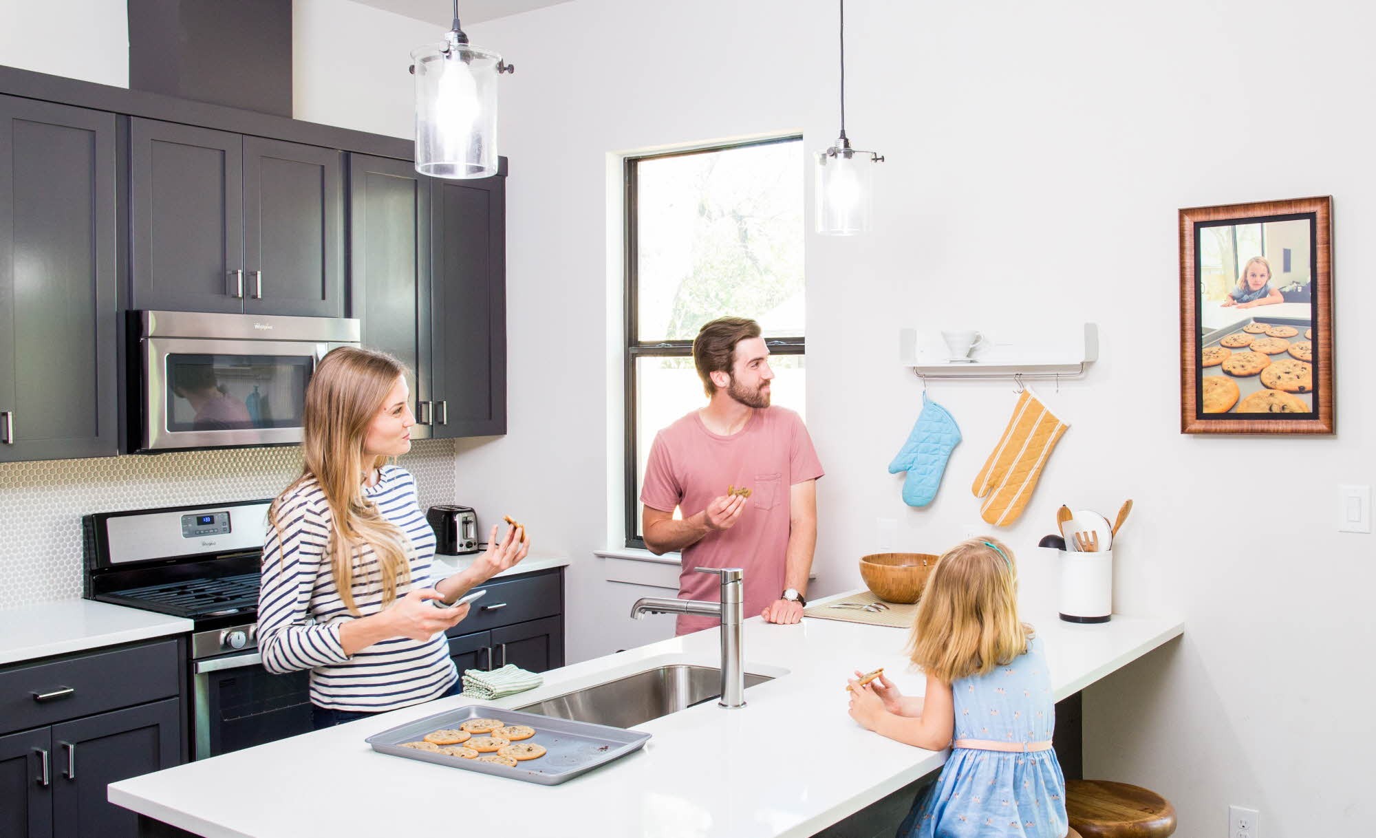 A family of three observe personal photos on their new digital frame by Acanvas in their kitchen.