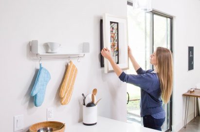 A woman effortlessly hangs up her new cord-free digital frame by Acanvas.