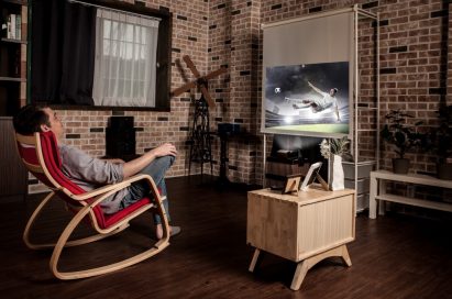 A man leans back in his chair while watching sport with the LG Minibeam projector
