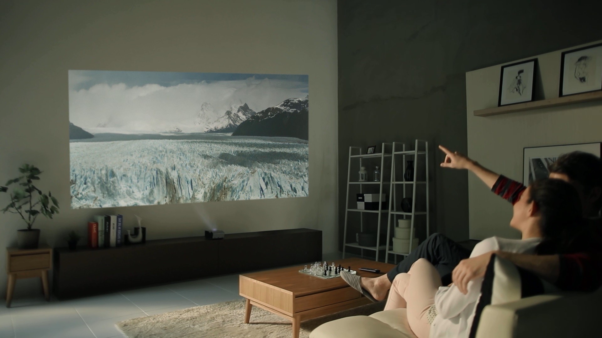 A couple sitting on a couch watching a scene of the Antarctic with the LG Minibeam projector