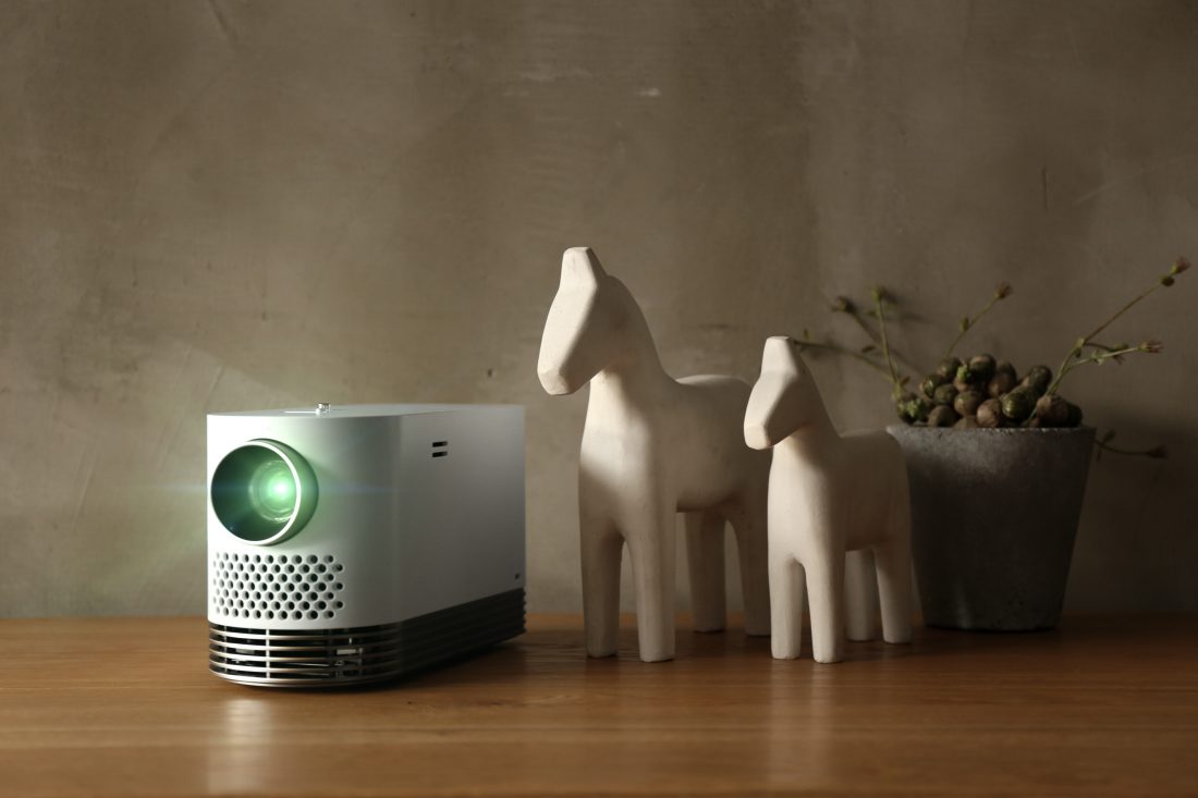 The LG Probeam Laser Projector (model HF80J) put on a table next to some decorative horses and a plant