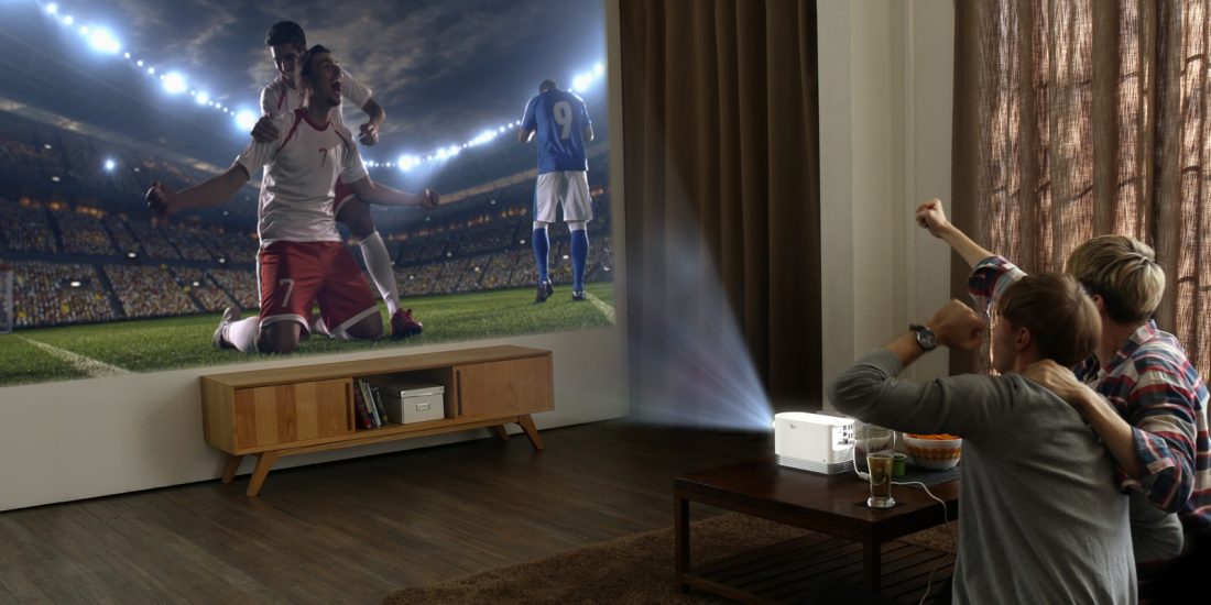 Two men watch a soccer game projected on the wall by the LG Probeam Laser Projector (model HF80J)