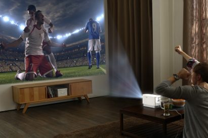 Two men watch a soccer game projected on the wall by the LG Probeam Laser Projector (model HF80J)