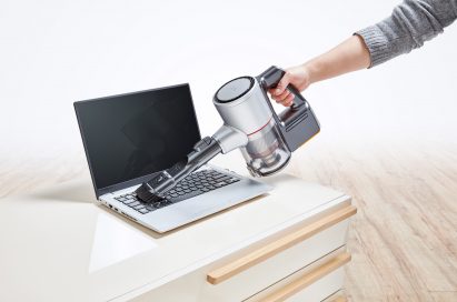 Close-up view of a person vacuuming a laptop keyboard with the LG CordZero Handstick