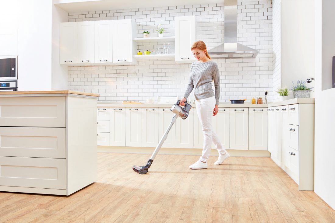 A woman vacuums a kitchen floor with the LG CordZero Handstick